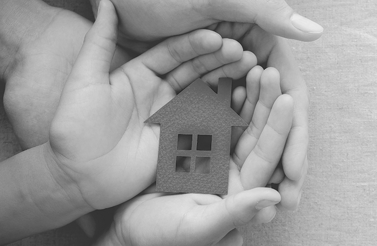 An adult's hands holding a child's hands who is holding a paper cutout of a house