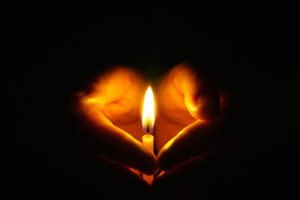 Close up of hands surrounding a lit candle in a dark room