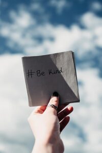 Hand holding a piece of paper with #Be Kind on it